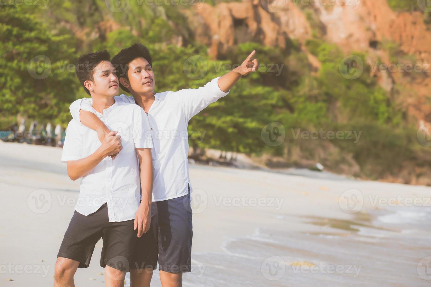 Homosexual portrait young asian couple standing pointing something together on beach in summer, asia gay going sea for leisure with romantic and happy in vacation at sea, LGBT with legal concept. photo