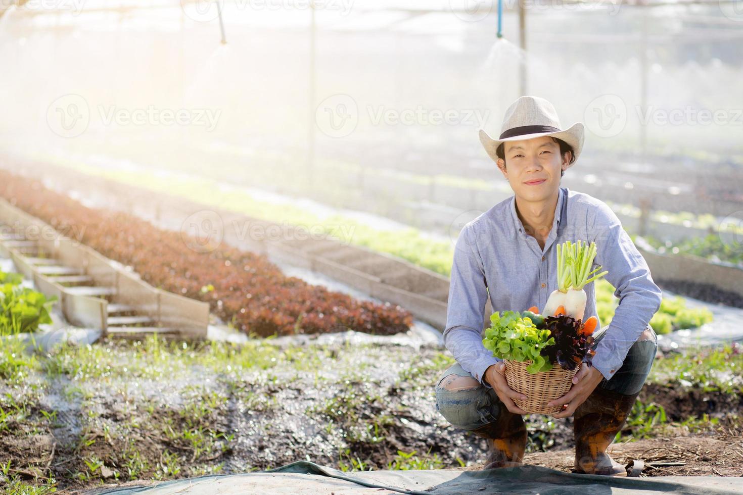 Portrait young asian man smiling harvest and picking up fresh organic vegetable kitchen garden in basket in the hydroponic farm, agriculture and cultivation for healthy food and business concept. photo