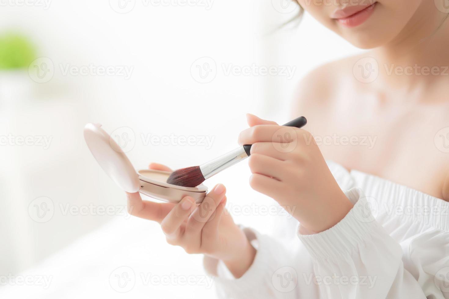 Beauty portrait young asian woman smiling with face looking mirror applying makeup with brush cheek in the bedroom, beautiful girl holding blusher facial, skin care and cosmetic concept. photo