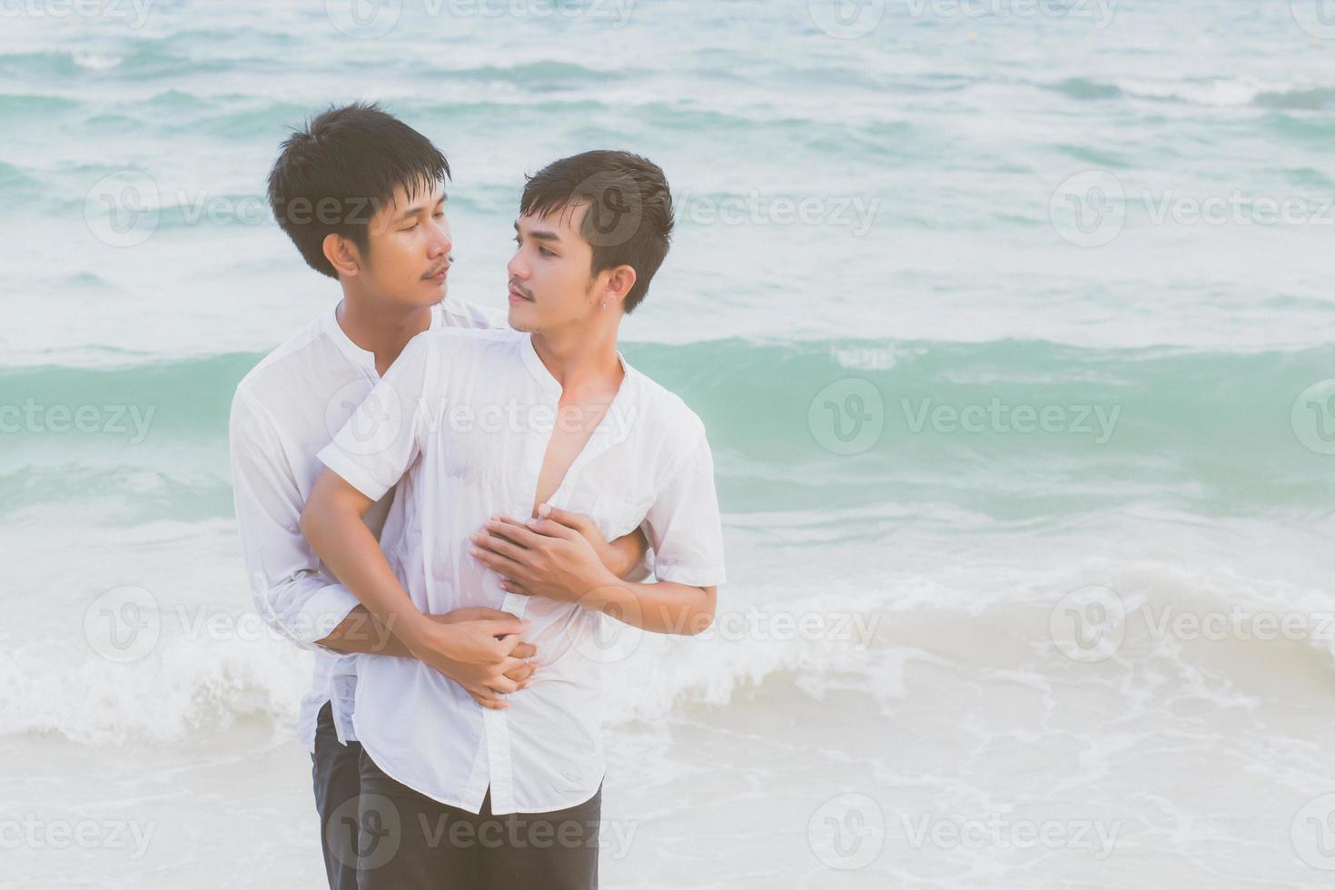 retrato homosexual joven pareja asiática de pie abrazo y miran juntos en la playa en verano, turismo gay de asia para el ocio y relajarse con romántico y feliz en vacaciones en el mar, concepto legal lgbt. foto