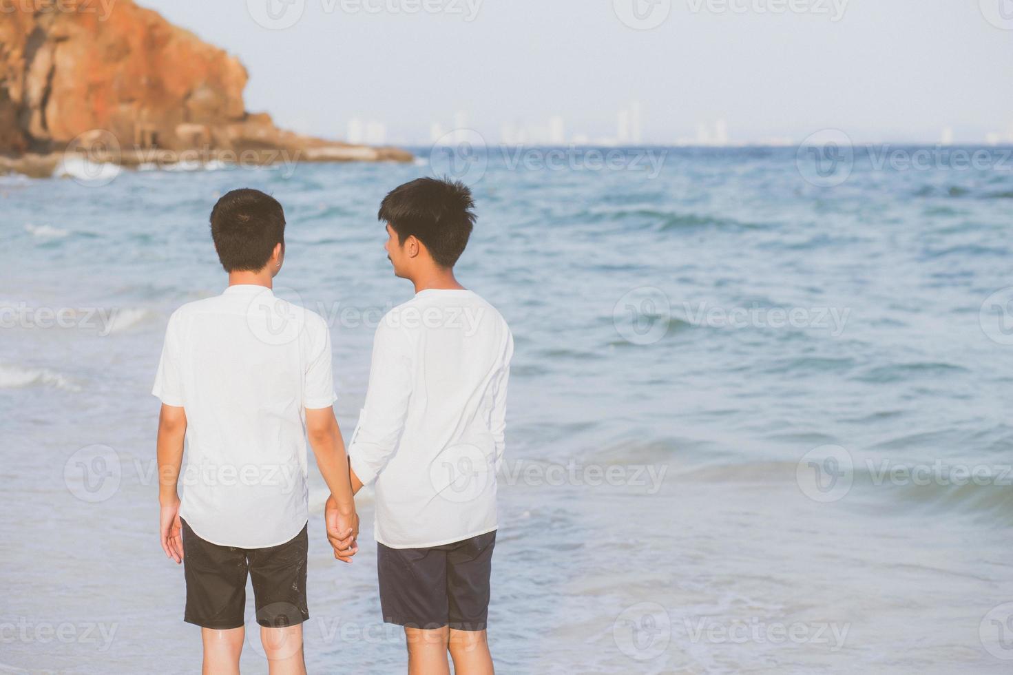 vista trasera retrato homosexual joven pareja asiática caminando alegremente juntos en la playa en verano, turismo gay de asia para el ocio y relajarse con felicidad en vacaciones en el mar, concepto legal lgbt. foto