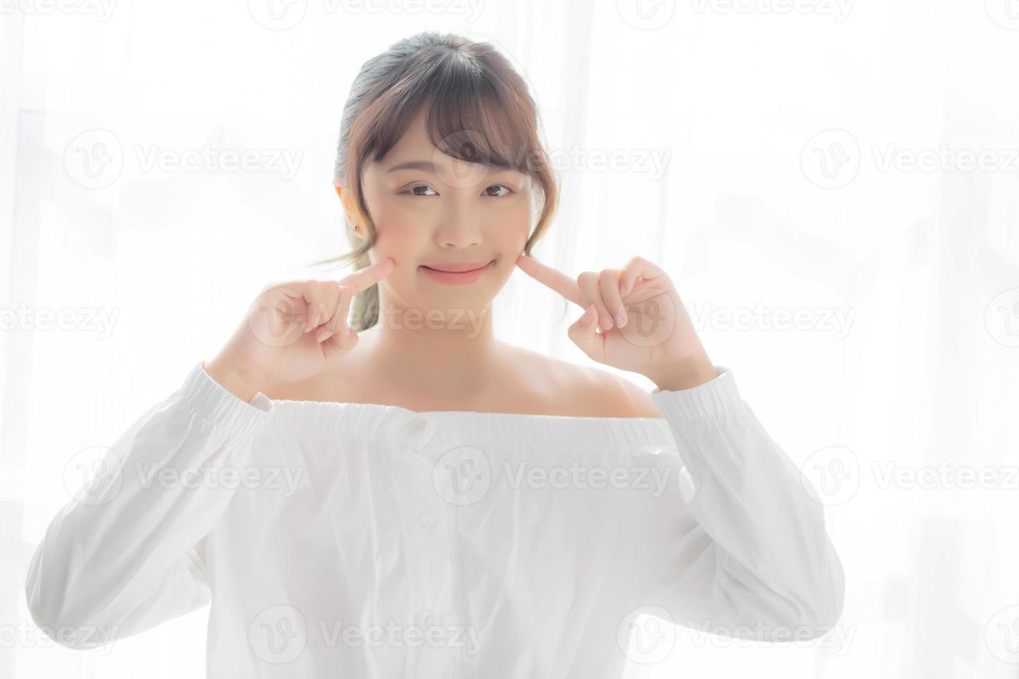 Beautiful portrait asian woman makeup of cosmetic, girl hand touch cheek and smile attractive, face beauty perfect with wellness in the bedroom with skin care and healthcare concept. photo
