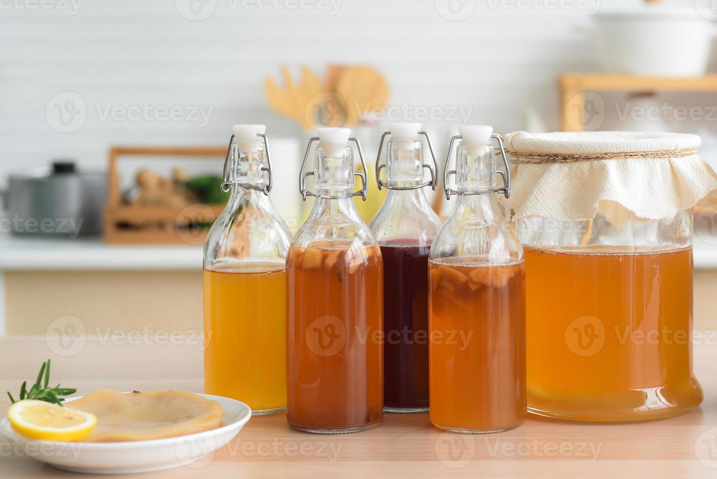 Té de kombucha crudo fermentado casero, variedad de sabores en botellas y frascos de vidrio mezclados con un jugo de fruta y scoby en una mesa de madera en la cocina. bebida probiótica natural saludable. foto