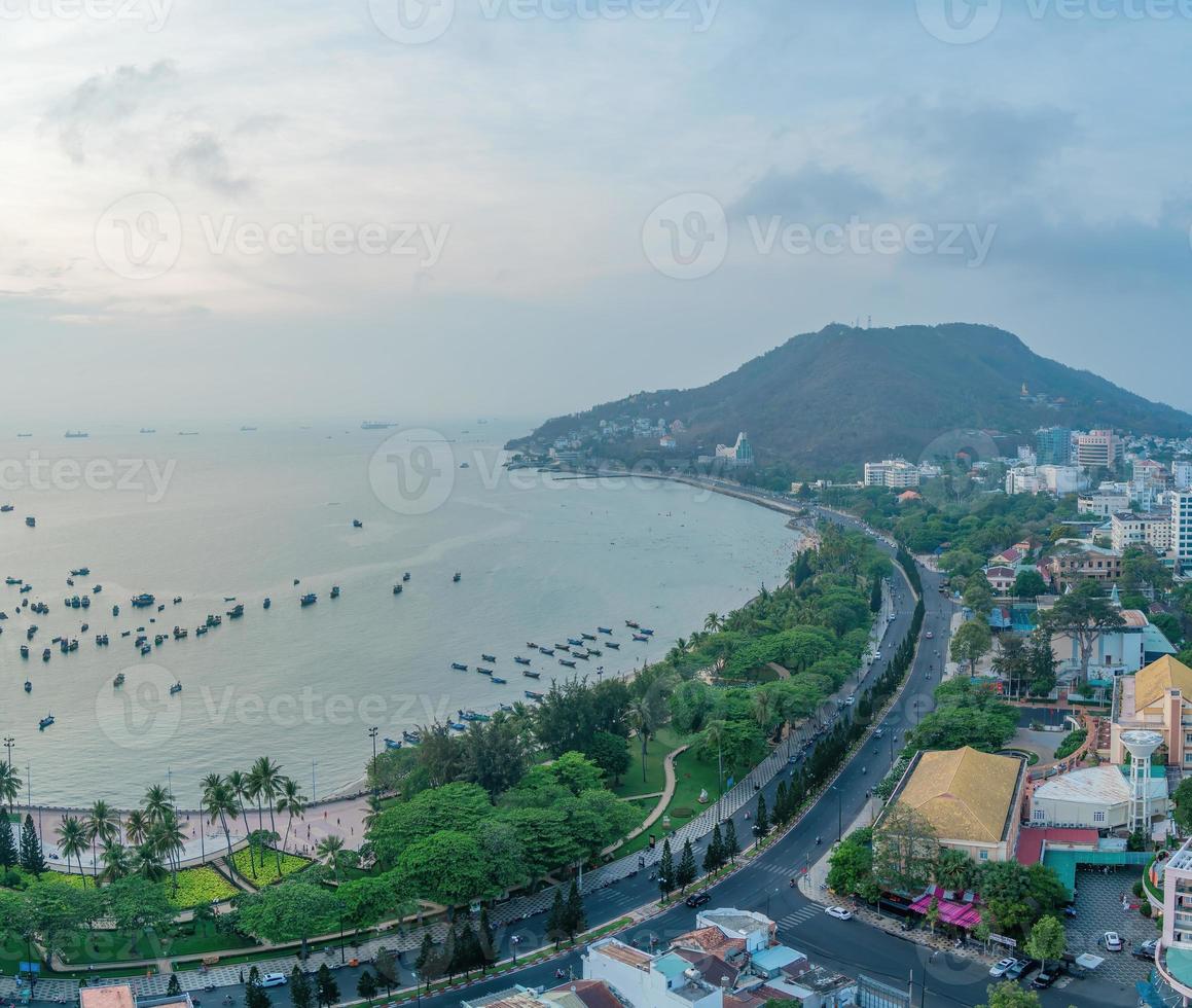 Vung Tau city aerial view with beautiful sunset and so many boats. Panoramic coastal Vung Tau view from above, with waves, coastline, streets, coconut trees and Tao Phung mountain in Vietnam. photo