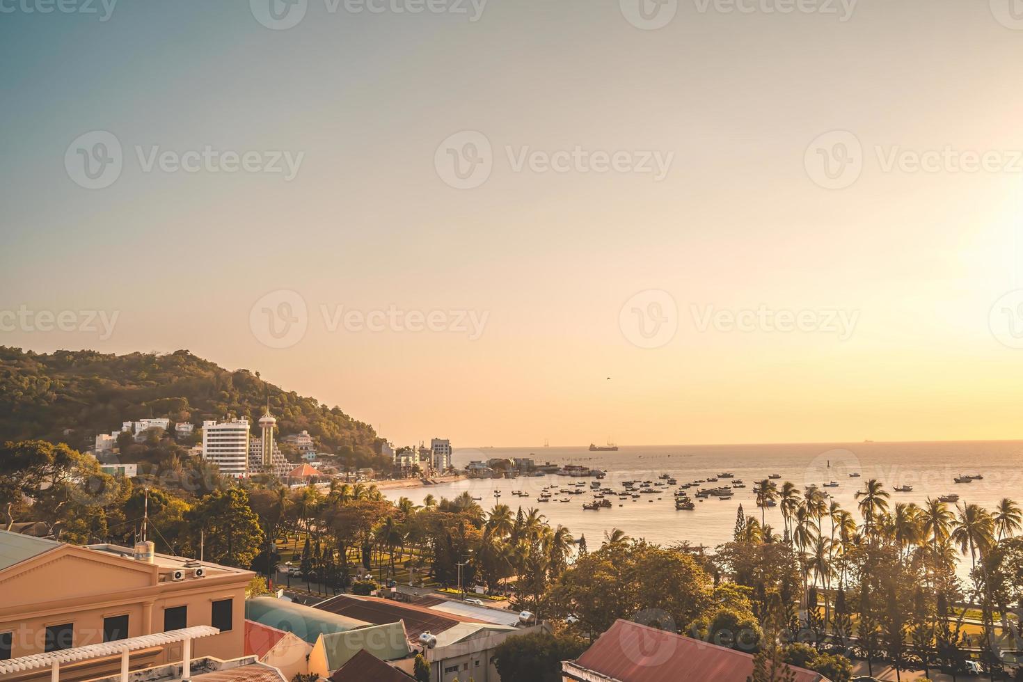 Vung Tau city aerial view with beautiful sunset and so many boats. Panoramic coastal Vung Tau view from above, with waves, coastline, streets, coconut trees and Tao Phung mountain in Vietnam. photo