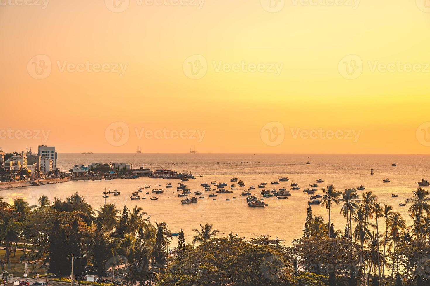 Vung Tau city aerial view with beautiful sunset and so many boats. Panoramic coastal Vung Tau view from above, with waves, coastline, streets, coconut trees and Tao Phung mountain in Vietnam. photo