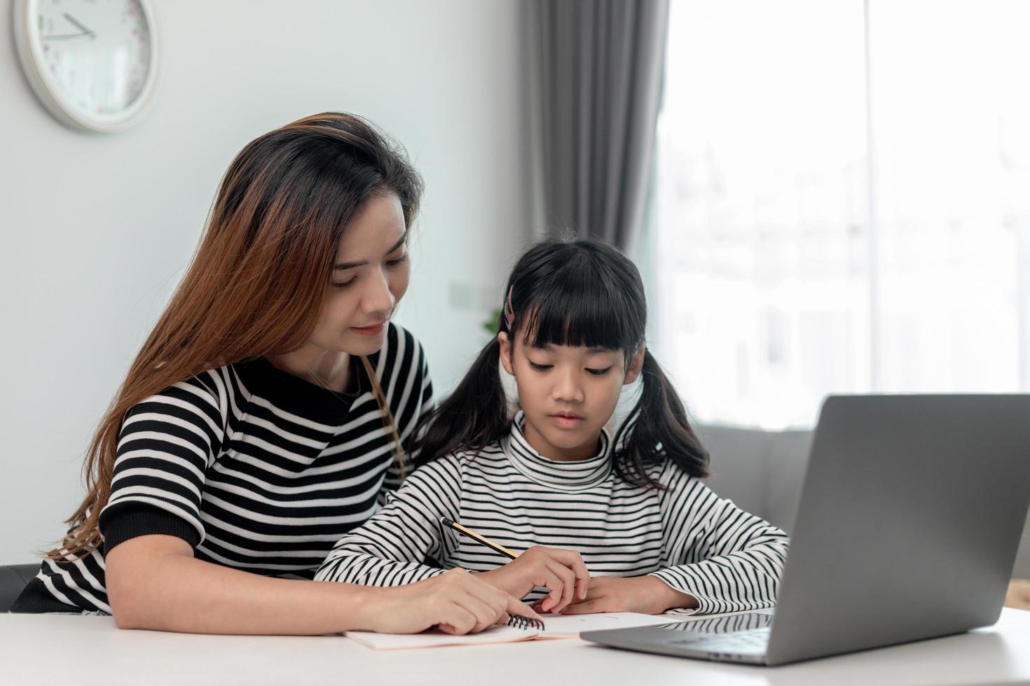 Asian little young girl kid learning online class at home with mother. Preschool child use laptop computer do homework, homeschool from school teacher by digital remote internet with support from mom. photo