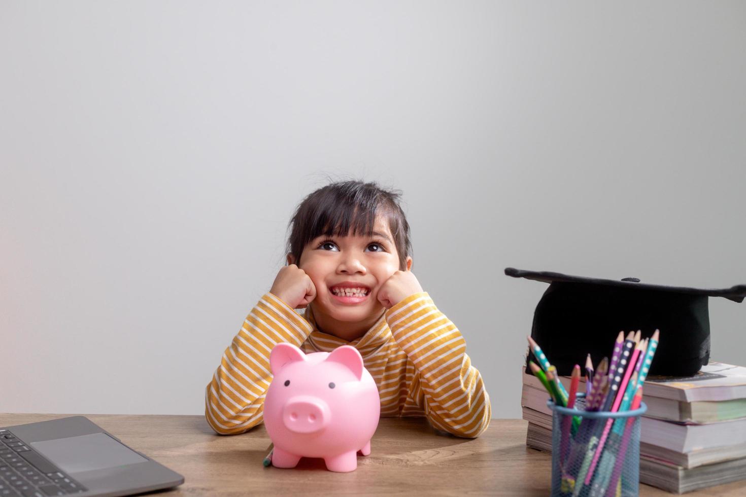 Asian little girl wearing a graduation cap with a pink piggy bank, Saving money, investment the future, photo