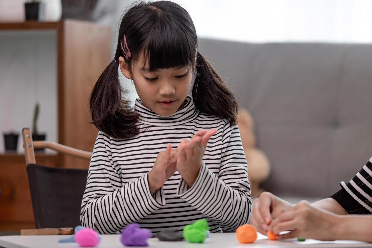 Asian mother and daughter play modeling clay together in kitchen with day light and they look happy. Concept of enjoy with family time photo