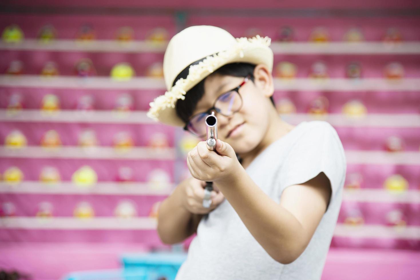 niño asiático feliz jugando a disparar con pistolas de muñecas en el evento local del festival del parque de diversión - gente con concepto de actividad feliz foto