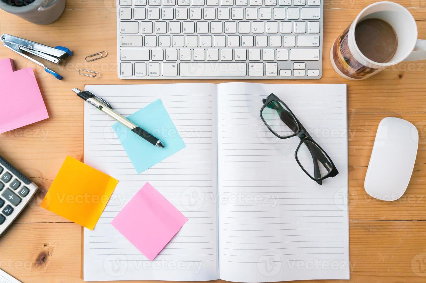 Top view on opened notebook,sticky note, cup of coffee ,keyboard other equipment on wooden office desk. photo