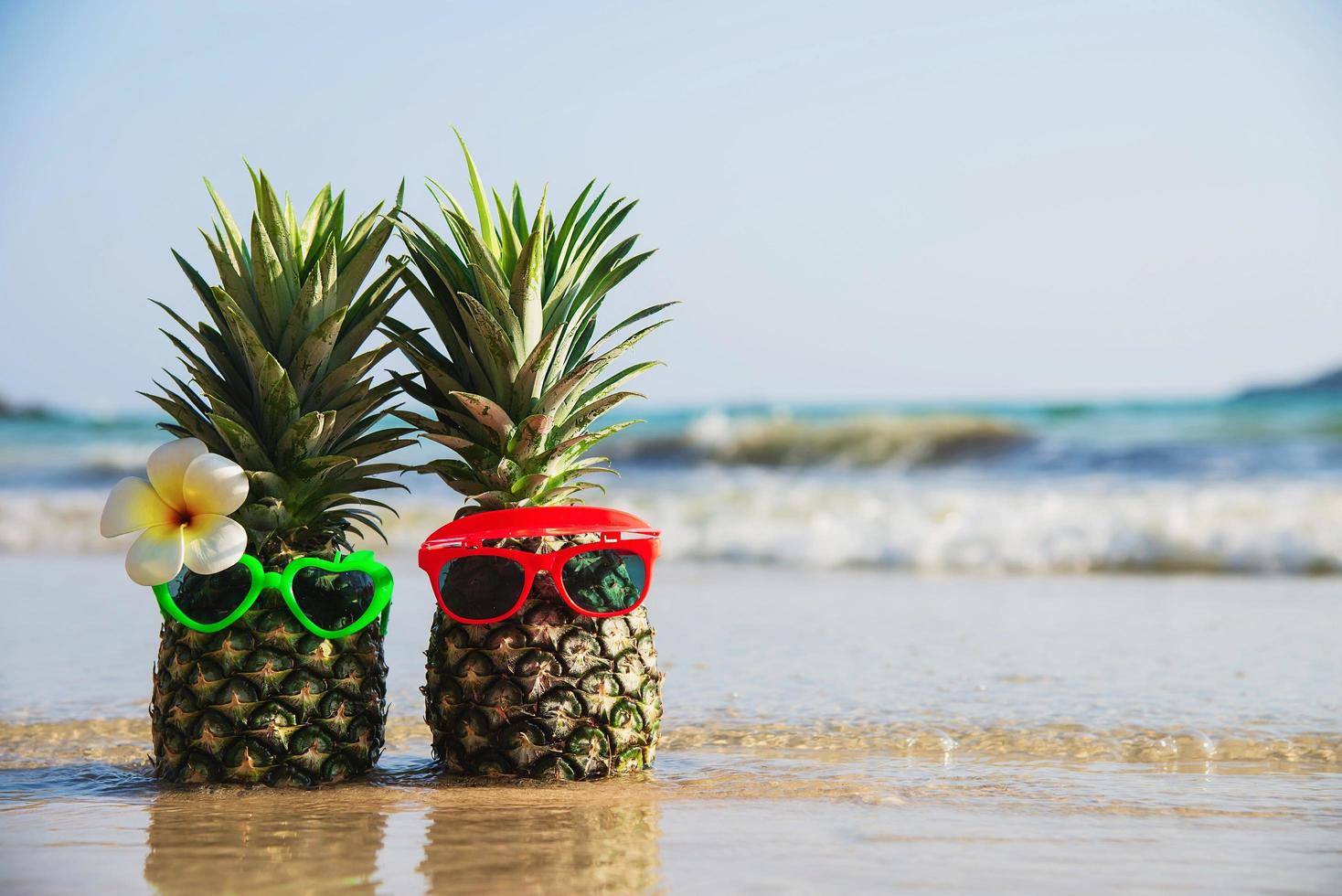 Lovely fresh couple pineapples putting glasses in tourist hands with sea wave background - happy love and fun with healthy vacation concept photo