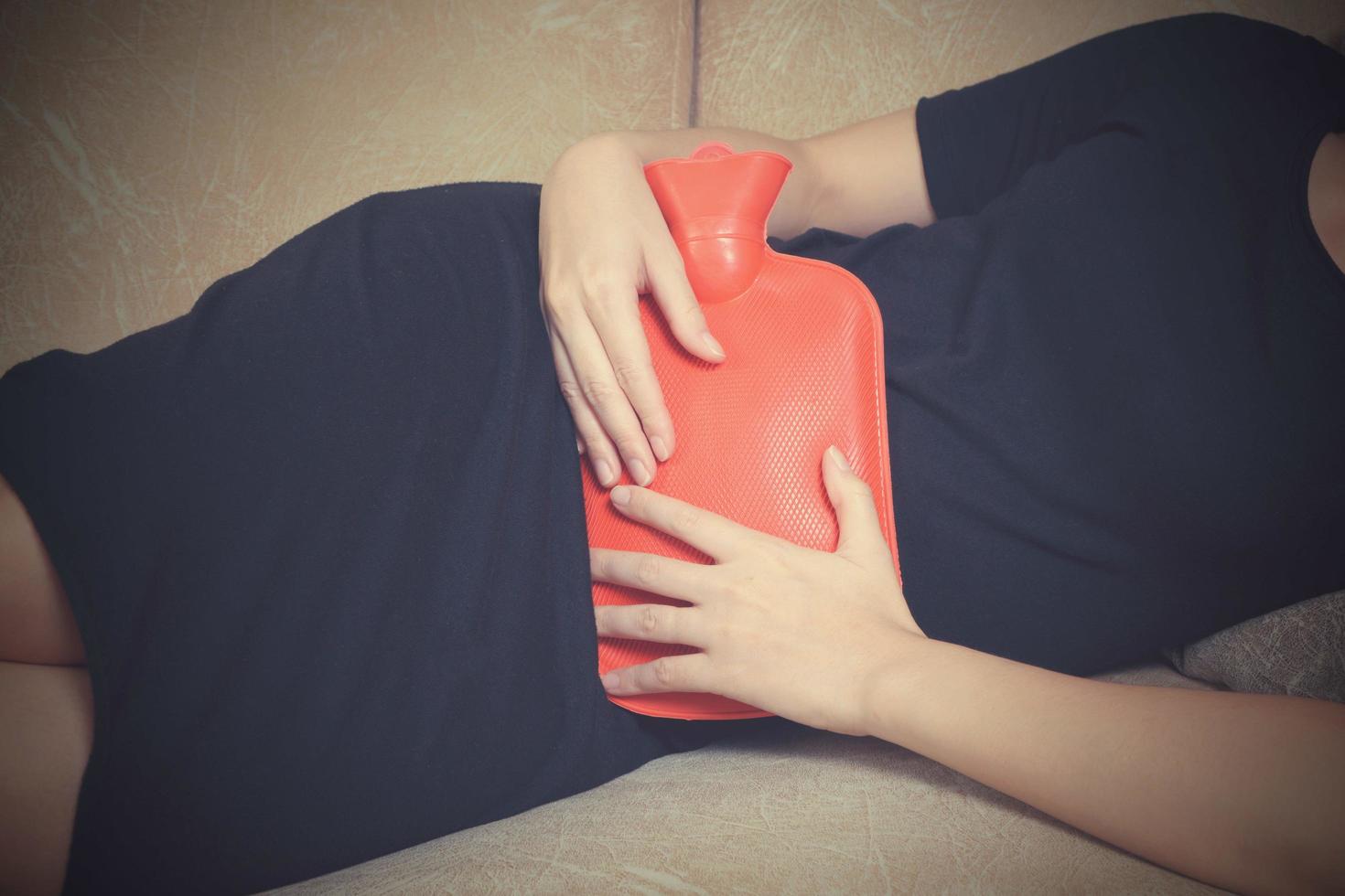 Sick woman lying on sofa with hot water bag and holding it on her belly with vintage tone photo