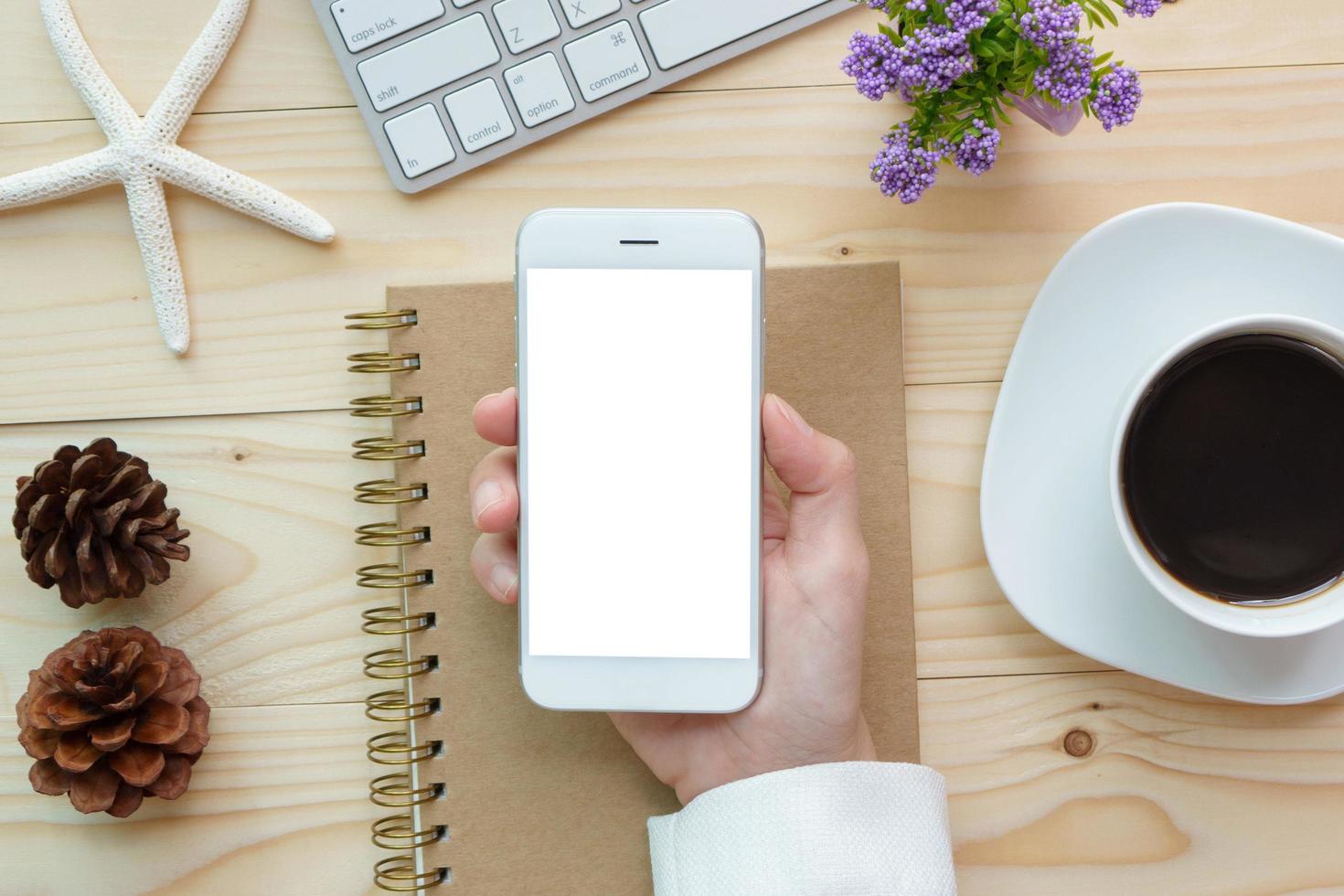 manos de mujer sosteniendo la pantalla vacía del teléfono inteligente en el trabajo de escritorio de madera. foto