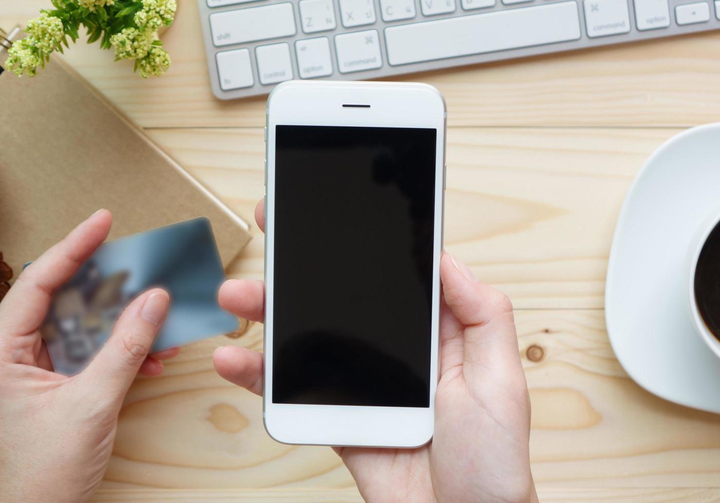 Female hands holding phone with blank screen and a credit card over the desk in the office photo