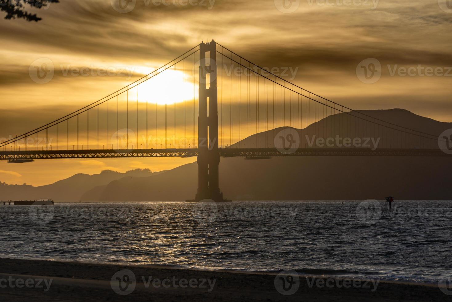 puesta de sol del puente golden gate y nubes amarillas doradas en el fondo y la bahía de san francisco en primer plano foto