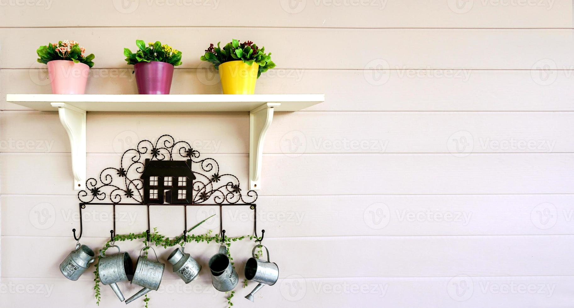 Flowers in three pots on a white shelf and hanging decoration small showers on white wooden wall background. photo