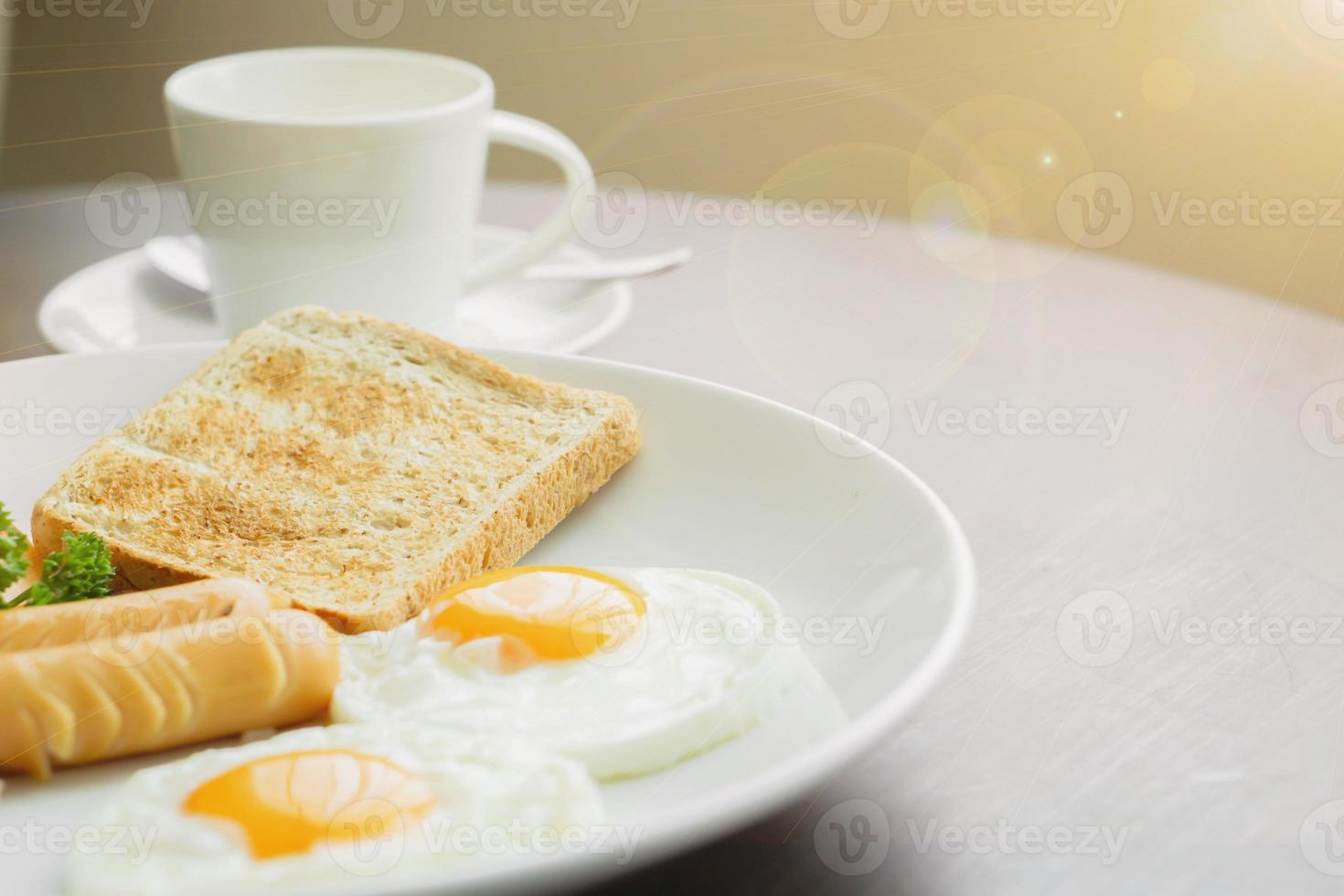 American breakfast and hot coffee in a white ceramic coffee cup on a wooden table with warm morning sunshine and lens flare background. photo