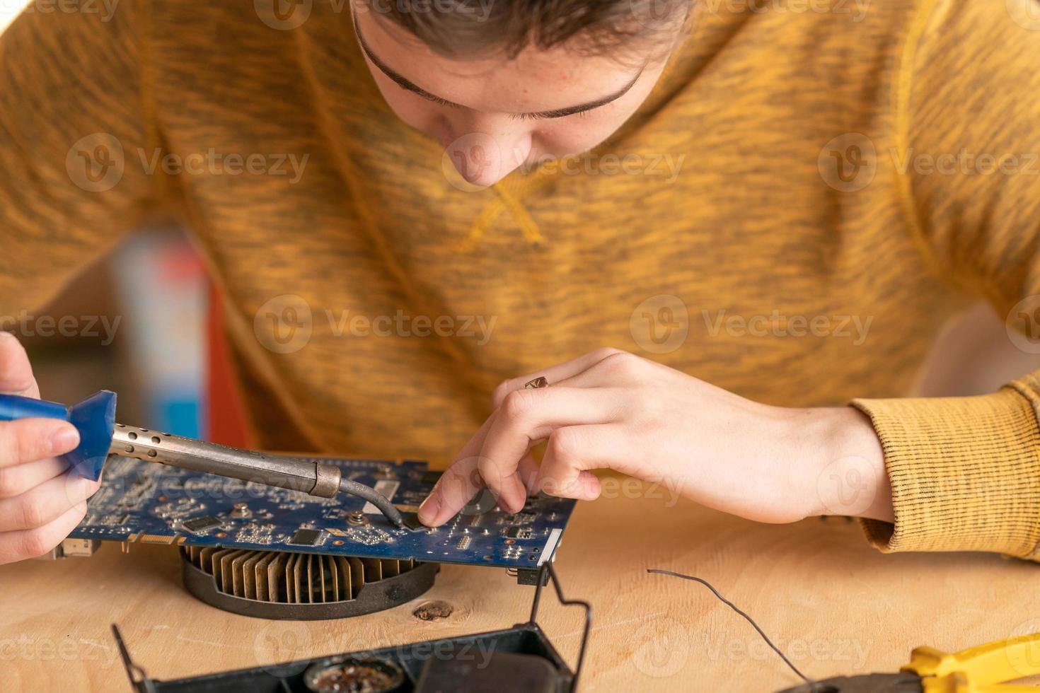 un joven suelda un microcircuito quemado con un soldador foto