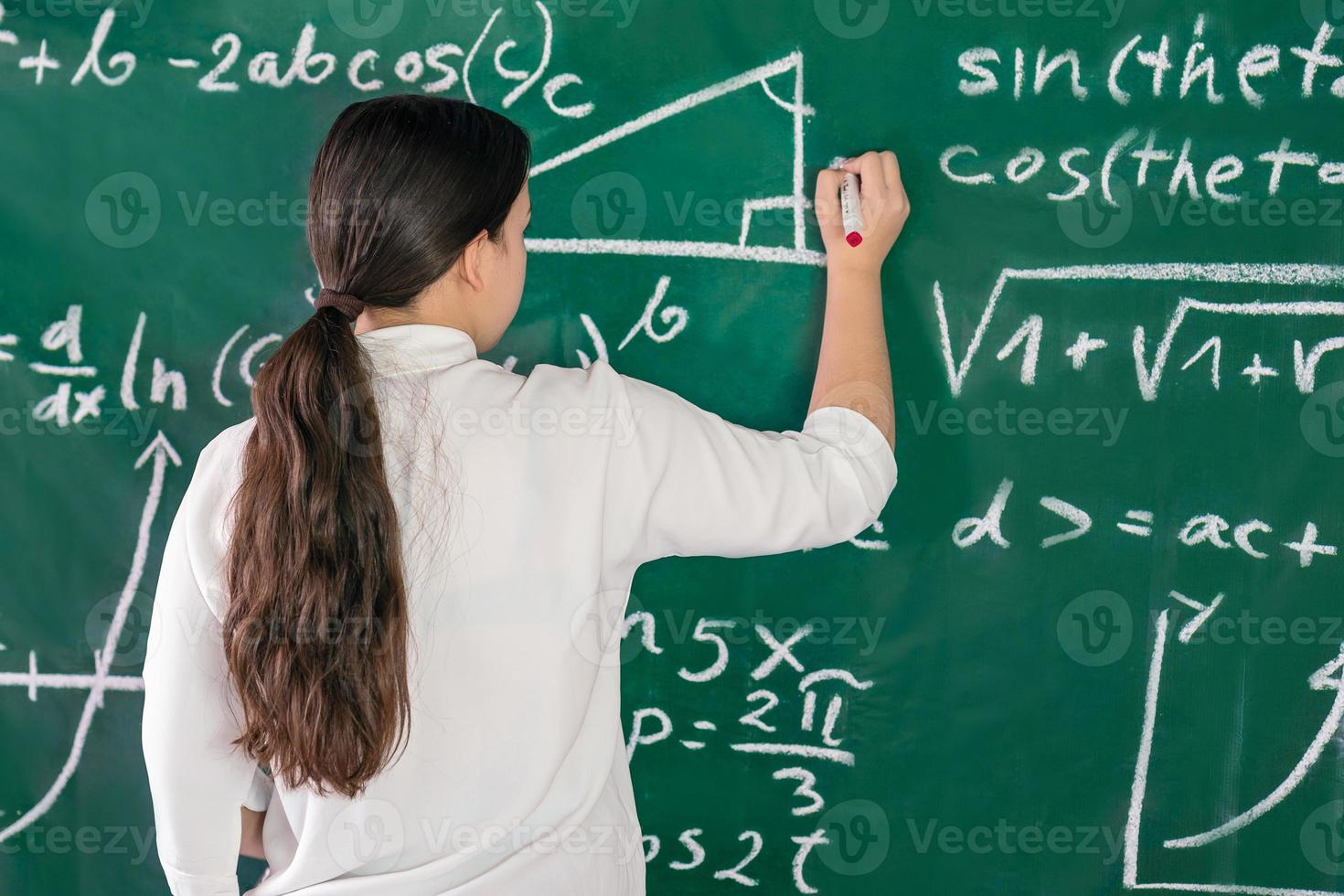 Girl writes mathematical examples on the school board. solves a geometry problem. photo