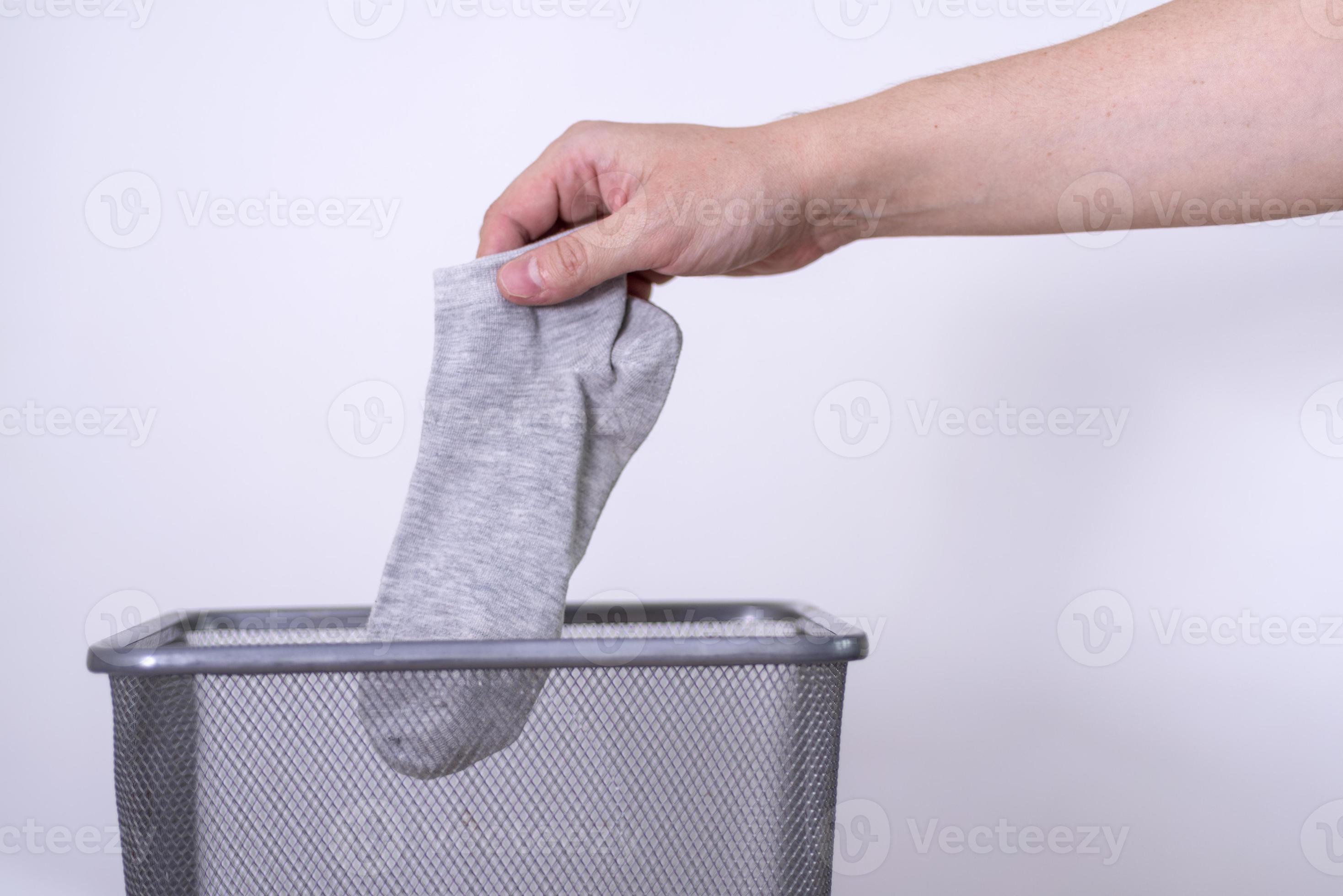 Man throwing an old sock with his hand into a trash can against a gray