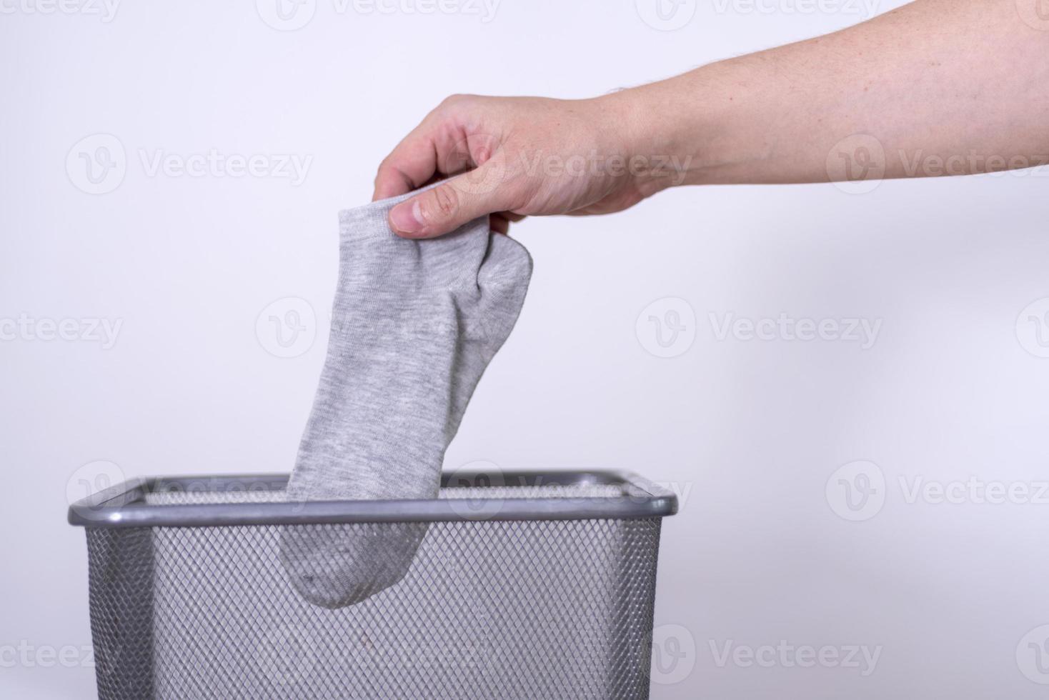 Man throwing an old sock with his hand into a trash can against a gray background. photo