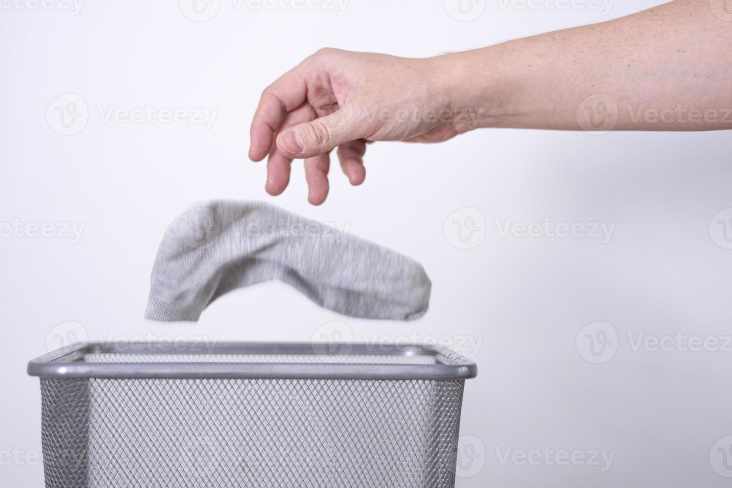 Man throwing an old sock with his hand into a trash can against a gray background. photo