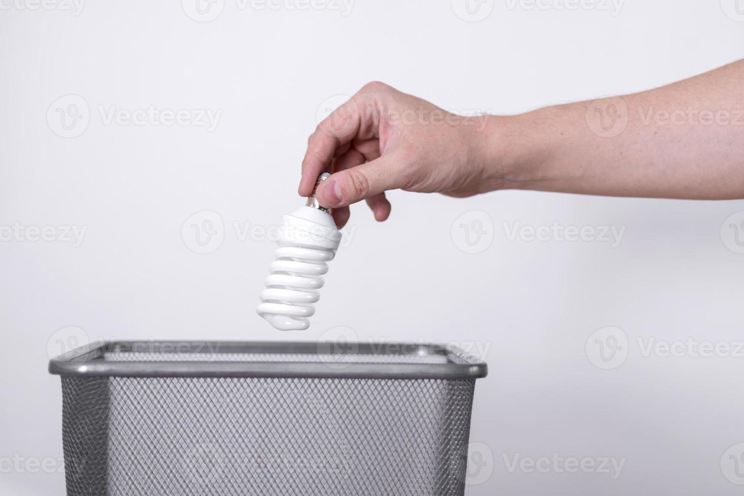 A hand throws a light bulb into a trash can against a gray background. photo