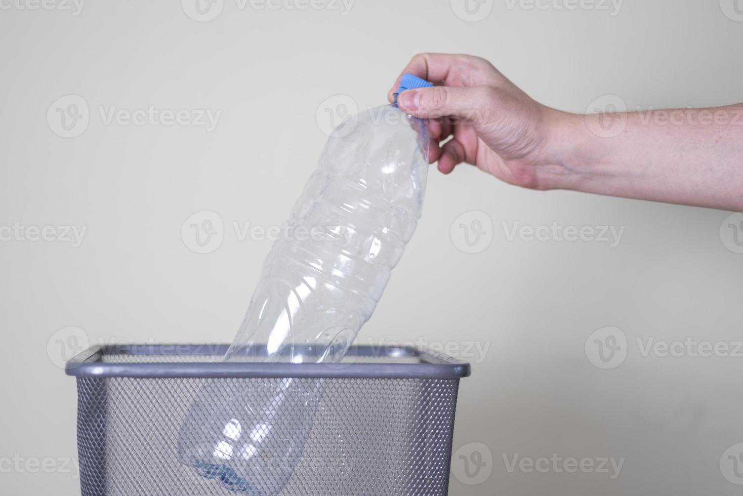 tirar una botella de plástico a la basura sobre un fondo gris. foto