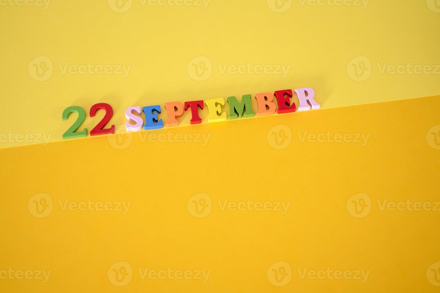 22 de septiembre sobre un fondo amarillo y de papel con letras y números de madera en diferentes colores. foto