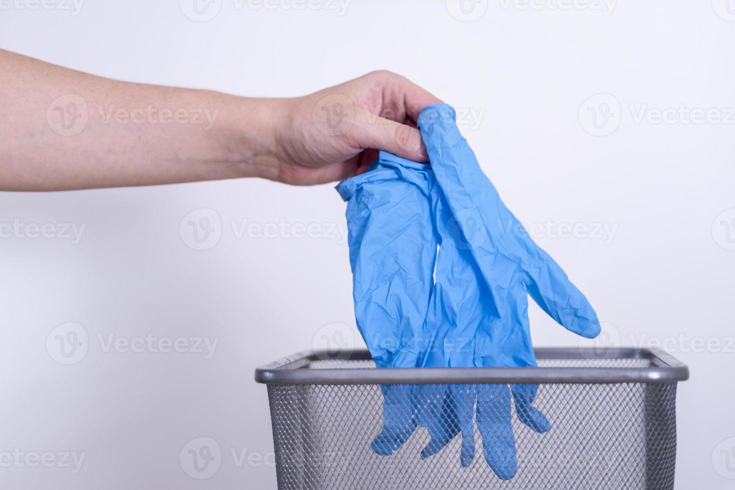 A man's hand throws blue medical gloves into a trash can against a gray background. photo