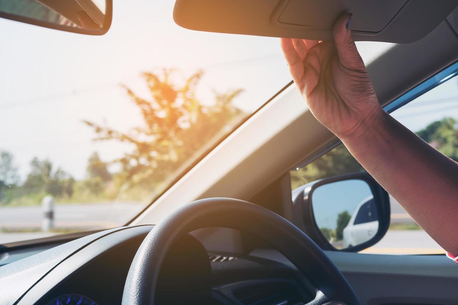 la señora ajusta la visera mientras conduce el automóvil en la carretera - automóvil interior usando el concepto foto