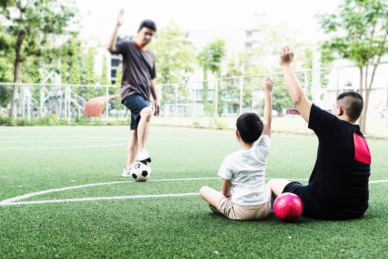 Dad coaches his children how to play soccer or football in green football field - outdoor family sport activity concept photo