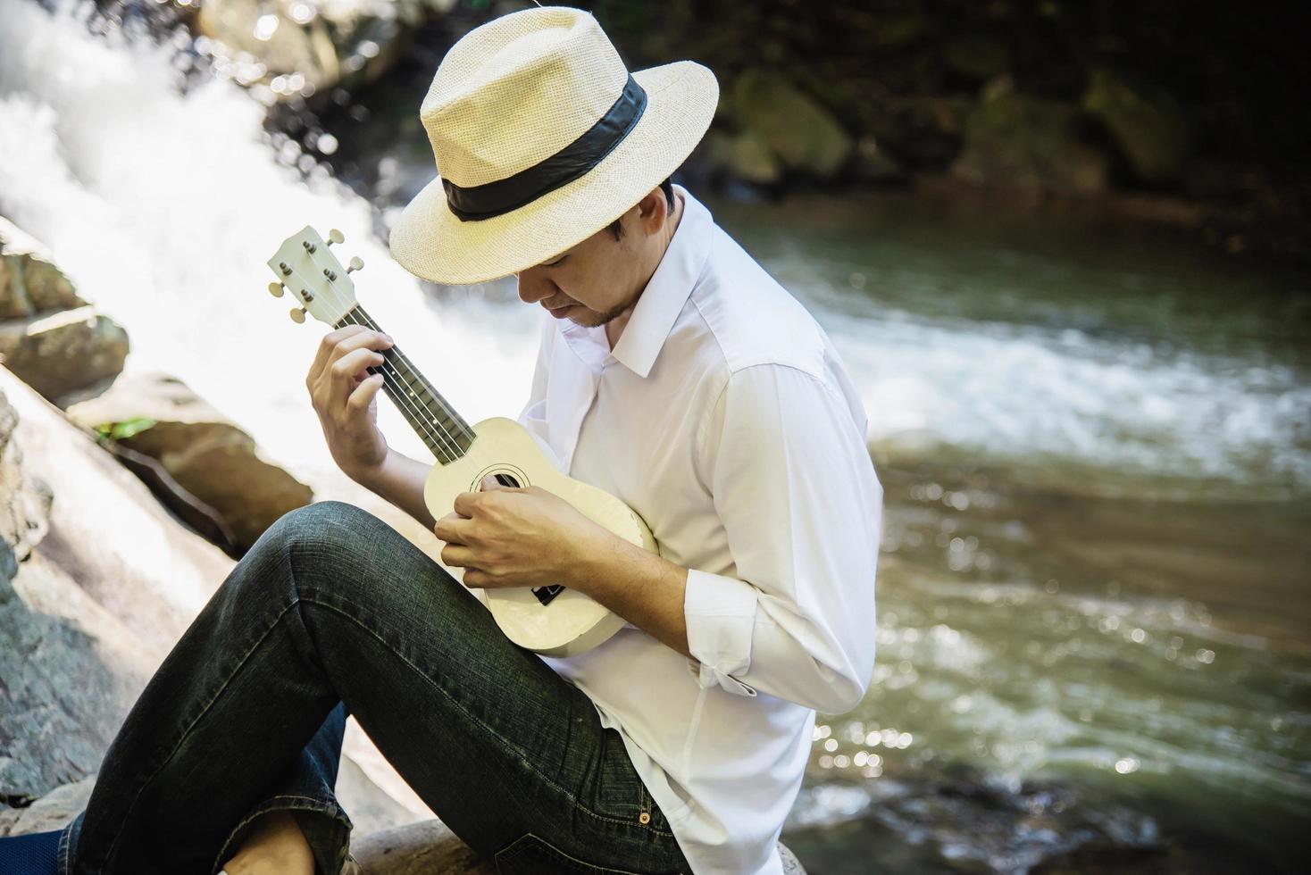 Man play ukulele new to the waterfall - people and music instrument life style in nature concept photo