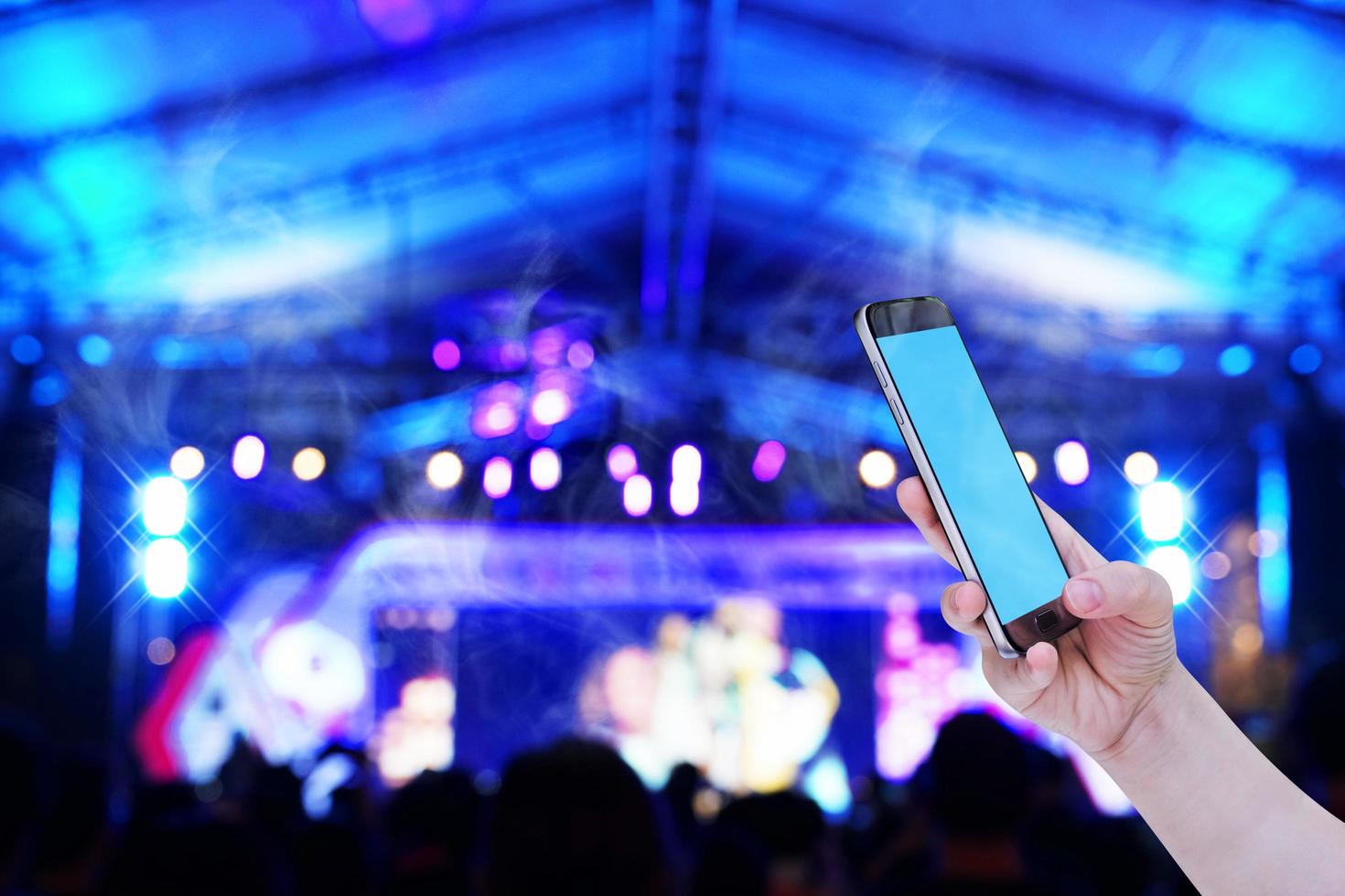 Hands holding mobile smartphone with light bokeh in concert blur background photo