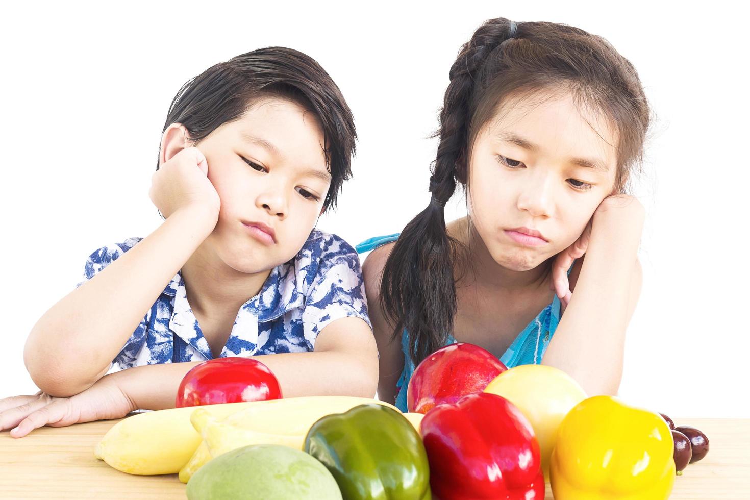 Asian boy and girl showing dislike expression with fresh colorful vegetables isolated over white background photo
