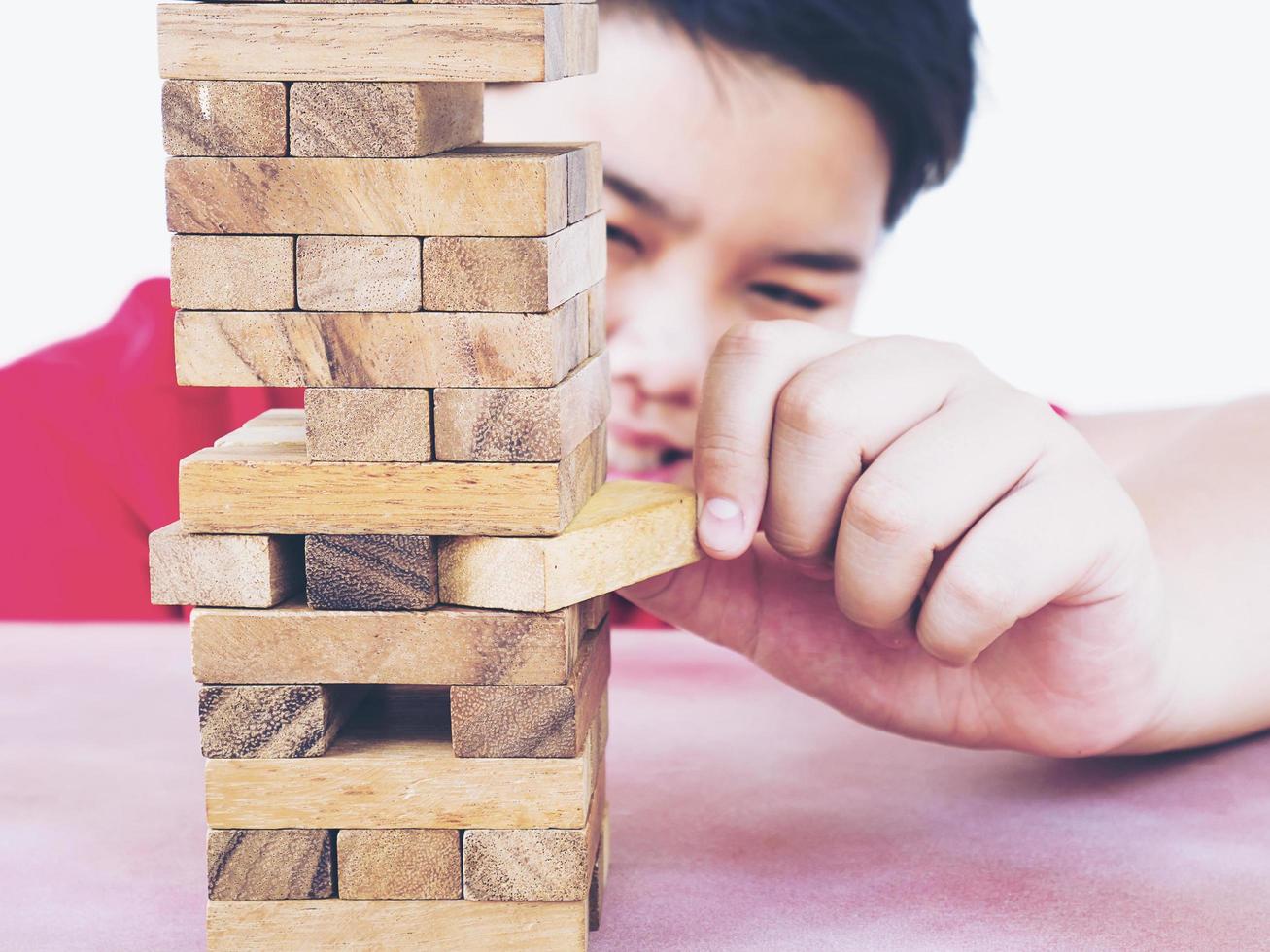 Asian kid is playing wood blocks tower game for practicing physical and mental skill. Photo is focused at model hands and isolated over white.