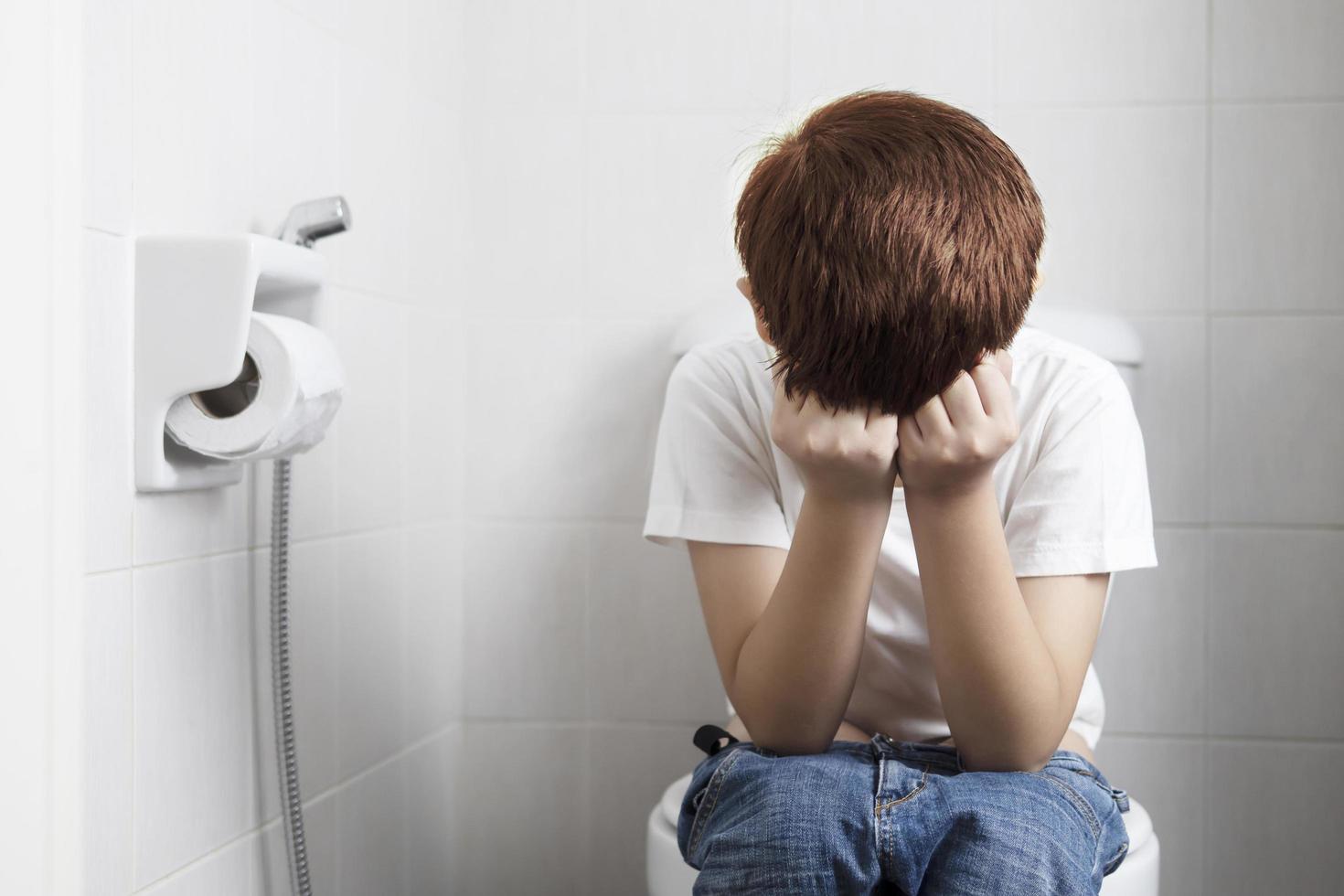 Asian boy sitting on toilet bowl holding tissue paper  - health problem concept photo