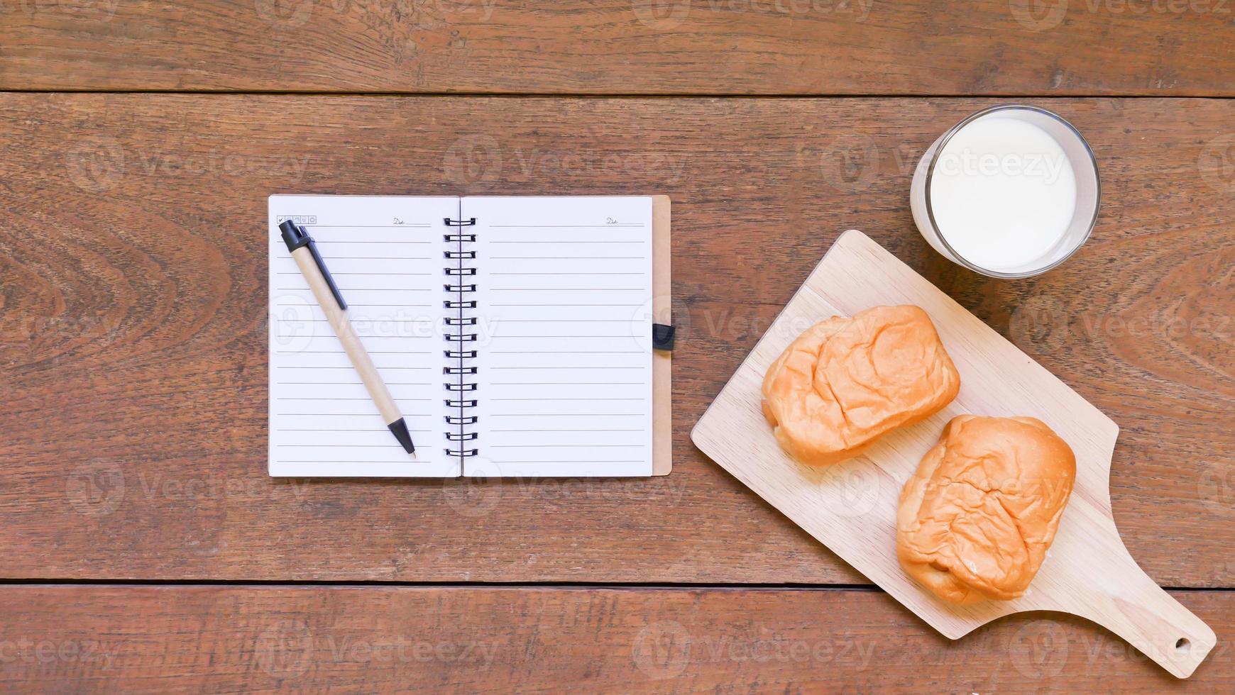 Notebook with bread and cup of milk on wooden table background. photo