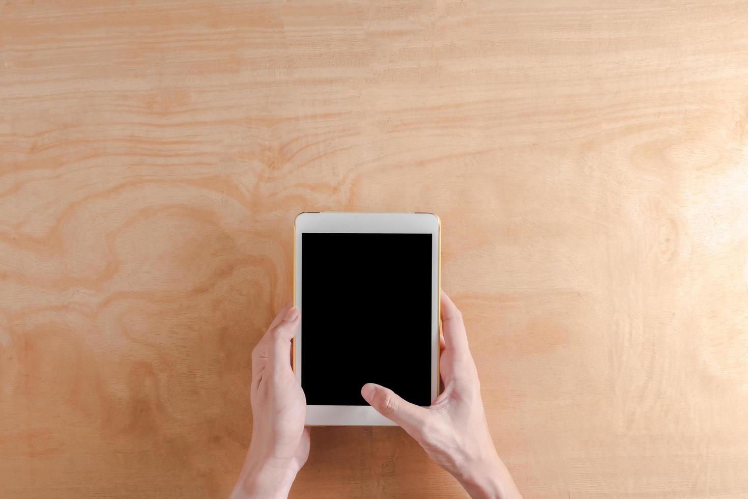 Top view of Male hands holdind tablet touch computer gadget on wooden background. photo