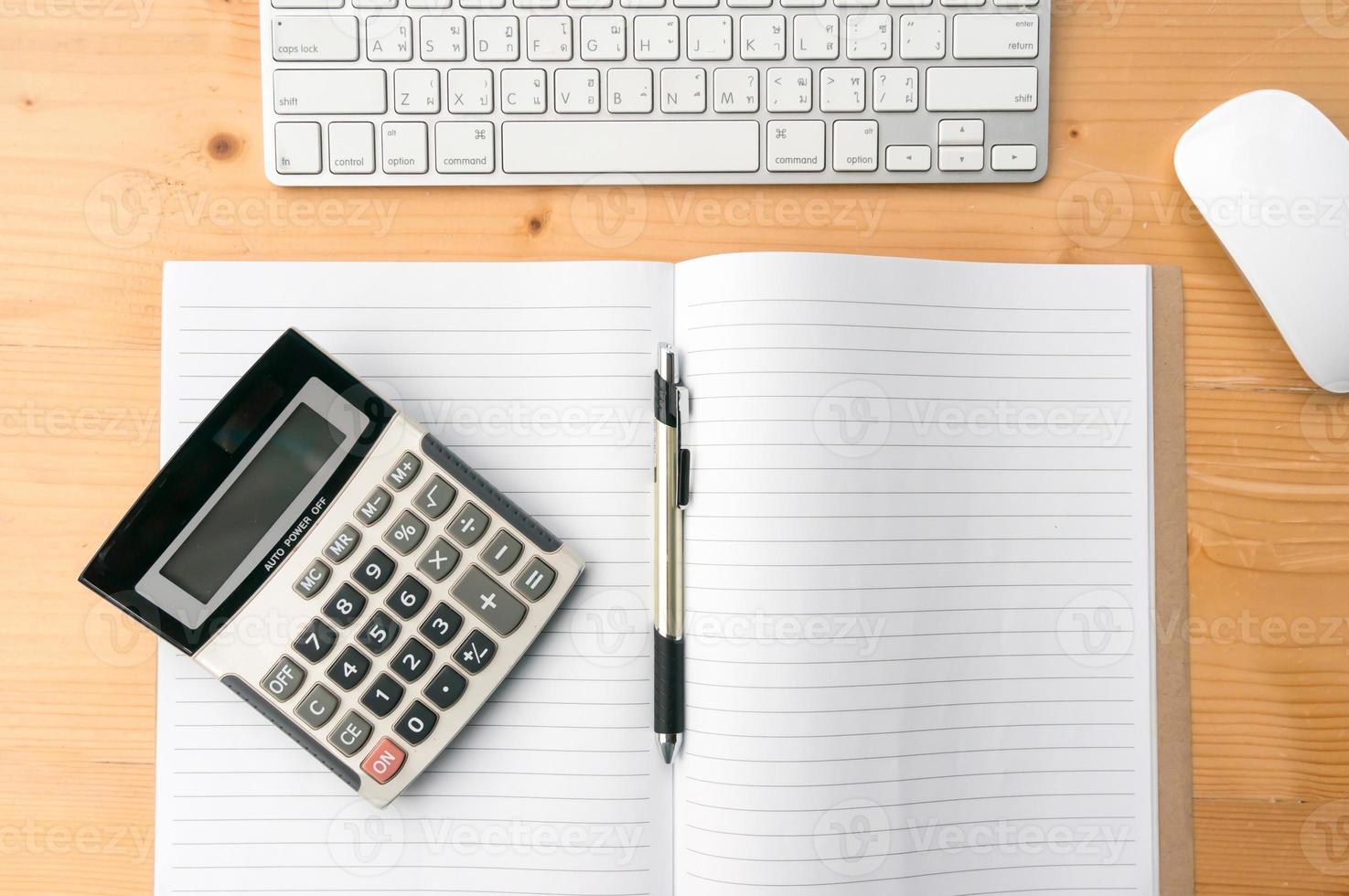 espacio de trabajo de vista superior con cuaderno en blanco, bolígrafo, teclado de calculadora y ratón sobre fondo de mesa de madera. foto