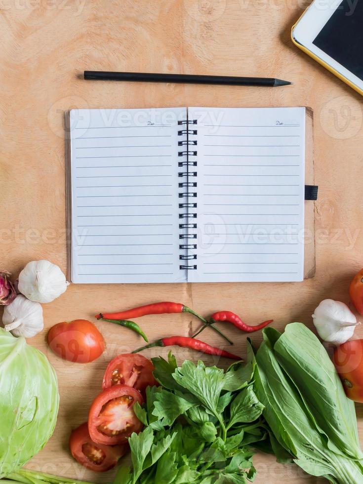 vista superior de verduras frescas con cuaderno en blanco sobre fondo de mesa de madera. foto