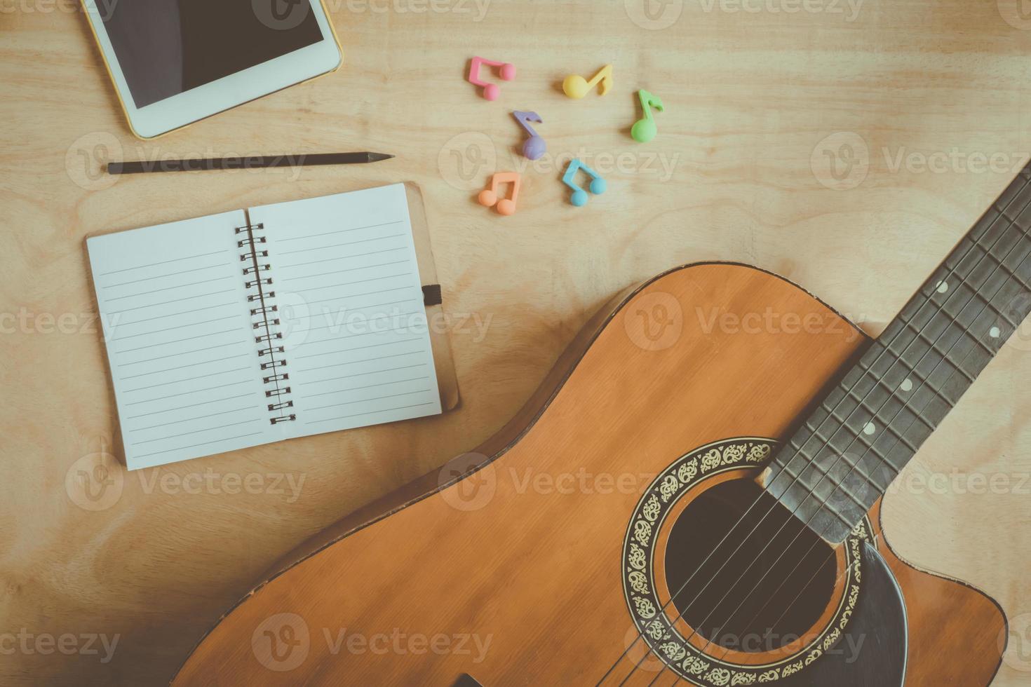 Top view of acoustic guitar with blank notebook on wooden table background.vintage effect style picture photo