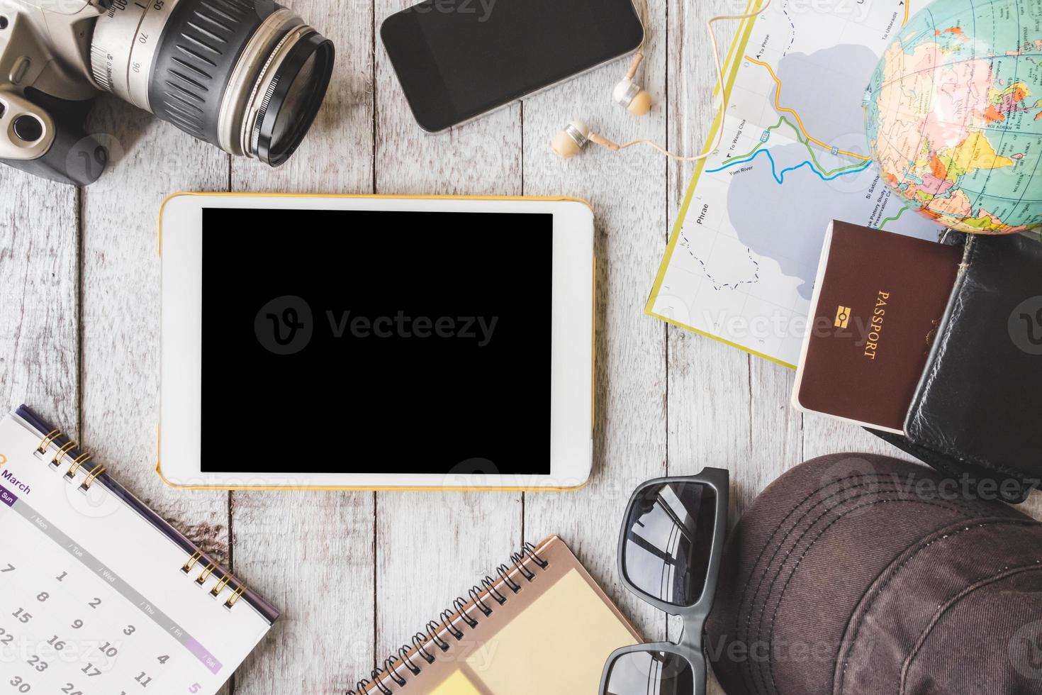 Top view of Tablet with camera,calendar,smart phone,earphones,sunglasses,cap,notebook,wallet,passport,map and globe on white wooden table background, Travel concept photo