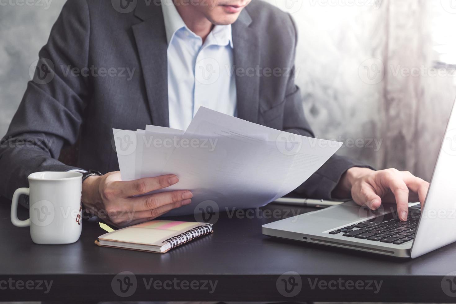 Close up of Businessman reading documents and working on laptop at the office. photo