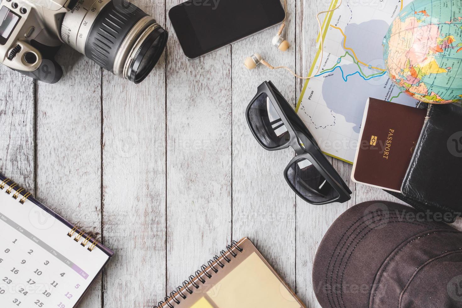 vista superior de la cámara con calendario, teléfono inteligente, auriculares, gafas de sol, gorra, cuaderno, billetera, pasaporte, mapa y globo sobre fondo de mesa de madera blanca, concepto de viaje foto