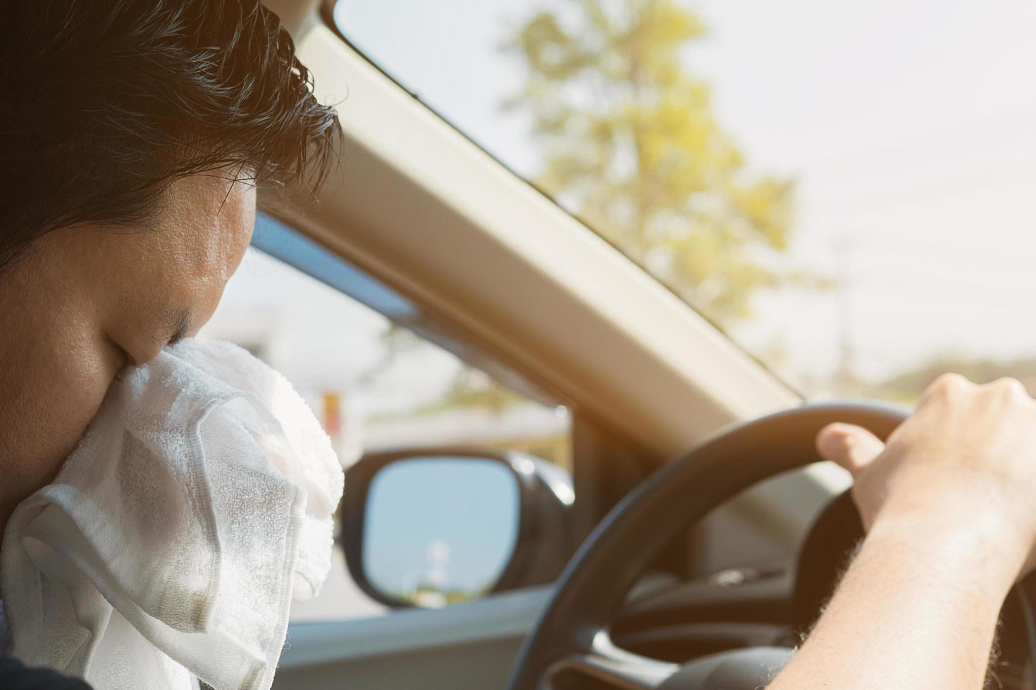 Tired man wiping his face using white cold refreshment cloth while driving a car - long journey driving with tired concept photo