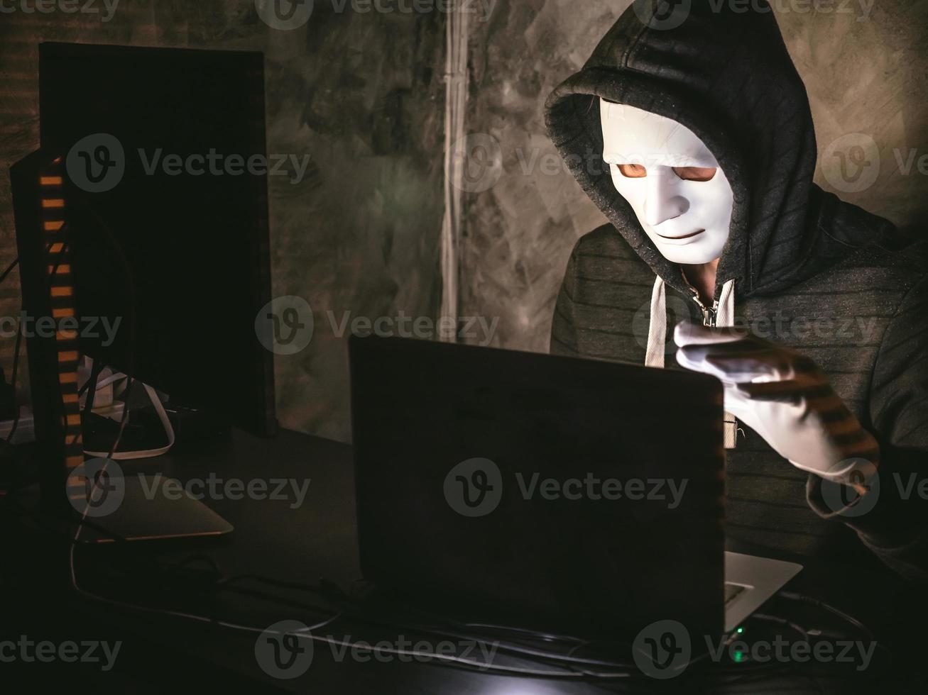 Computer hacker - Man in hoodie shirt with mask stealing data from laptop photo