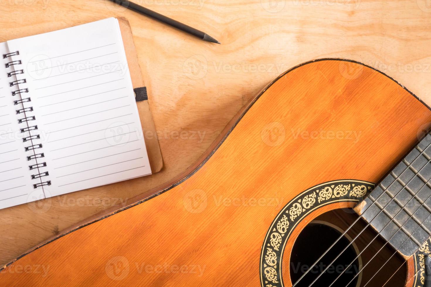 Top view of acoustic guitar with blank notebook on wooden table background. photo