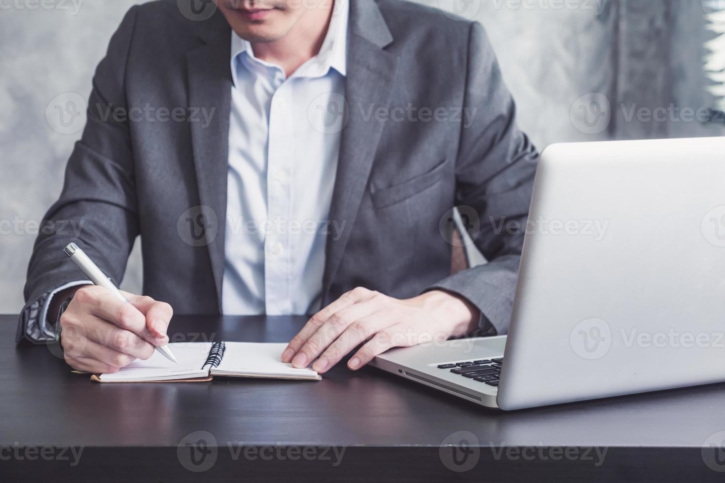 Close up of Businessman writing some data in notebook and working on laptop at the office. photo